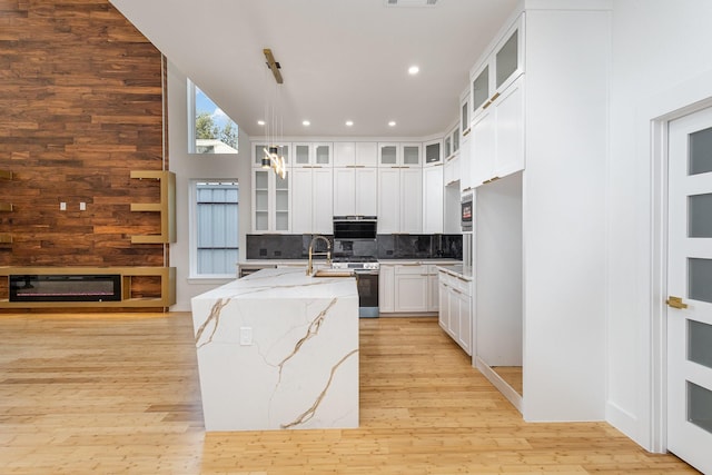 kitchen featuring tasteful backsplash, stainless steel range with gas stovetop, white cabinetry, a kitchen island with sink, and light stone counters