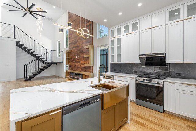 kitchen with light stone counters, white cabinets, hanging light fixtures, and appliances with stainless steel finishes