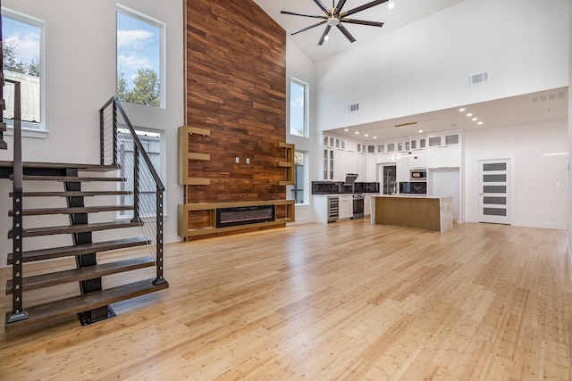 unfurnished living room with ceiling fan, light hardwood / wood-style floors, and a towering ceiling