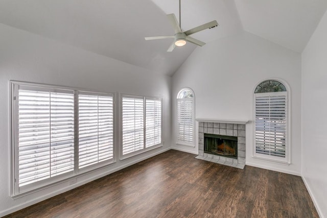 unfurnished living room featuring ceiling fan, dark wood-type flooring, a tile fireplace, and high vaulted ceiling