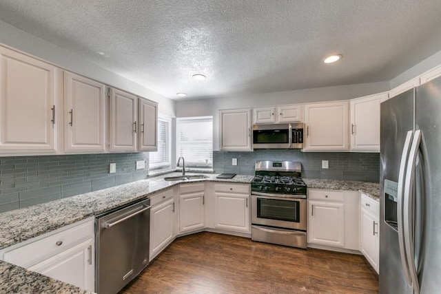 kitchen featuring white cabinetry, stainless steel appliances, dark hardwood / wood-style floors, backsplash, and light stone countertops