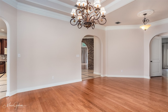 empty room with crown molding, a chandelier, and light wood-type flooring