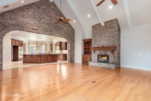 unfurnished living room featuring beamed ceiling, a fireplace, ceiling fan, high vaulted ceiling, and light hardwood / wood-style flooring