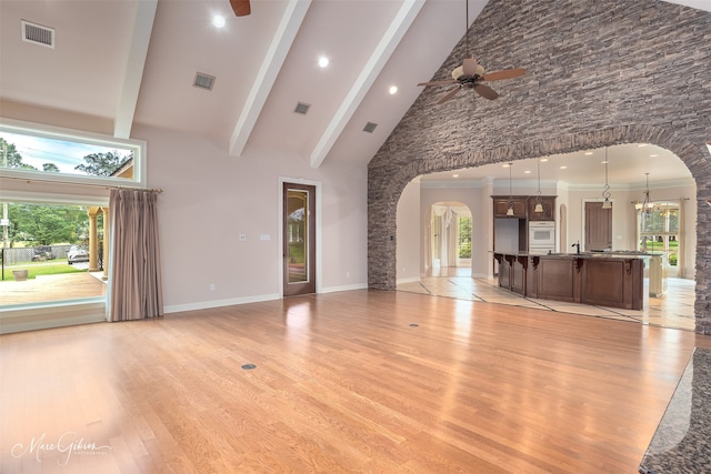 unfurnished living room featuring high vaulted ceiling, a healthy amount of sunlight, beamed ceiling, and ceiling fan with notable chandelier