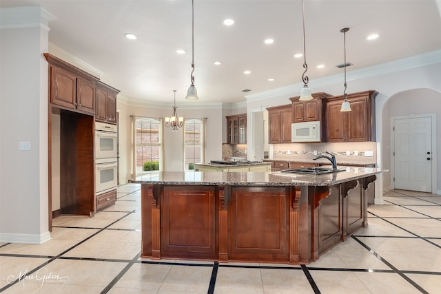 kitchen featuring pendant lighting, white appliances, dark stone counters, sink, and a kitchen island with sink