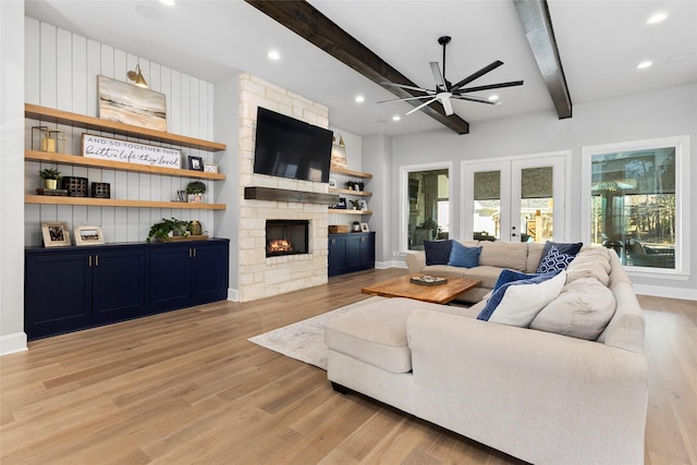 living room with french doors, a fireplace, beamed ceiling, light wood-type flooring, and ceiling fan