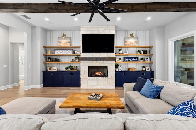 living room with ceiling fan, a fireplace, beam ceiling, and light wood-type flooring