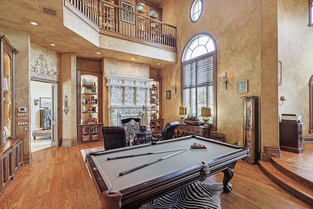 game room with visible vents, a fireplace, a towering ceiling, and wood finished floors