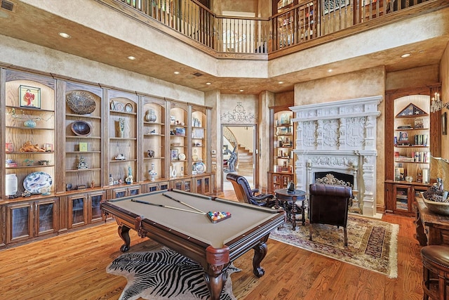 playroom featuring wood-type flooring, billiards, a towering ceiling, and a fireplace