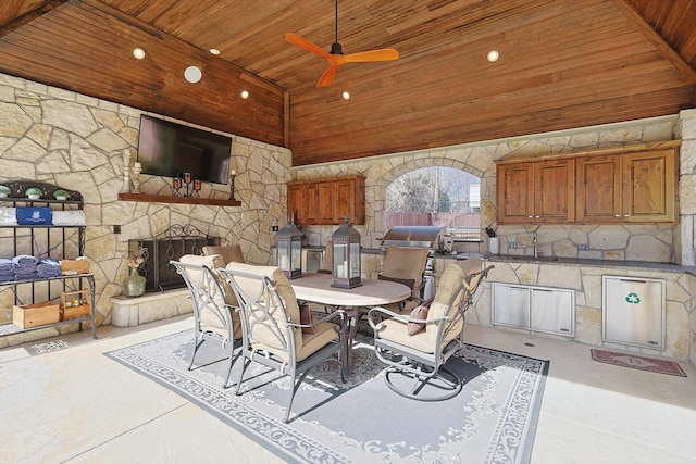 view of patio with an outdoor kitchen, an outdoor stone fireplace, outdoor dining area, and a ceiling fan