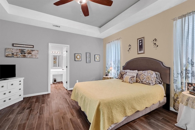 bedroom featuring ensuite bathroom, ceiling fan, dark hardwood / wood-style flooring, and a tray ceiling