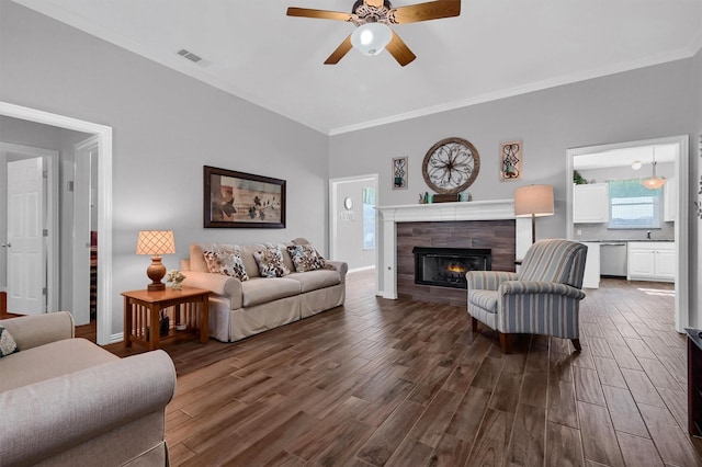 living room with ceiling fan, dark hardwood / wood-style floors, ornamental molding, and a tiled fireplace