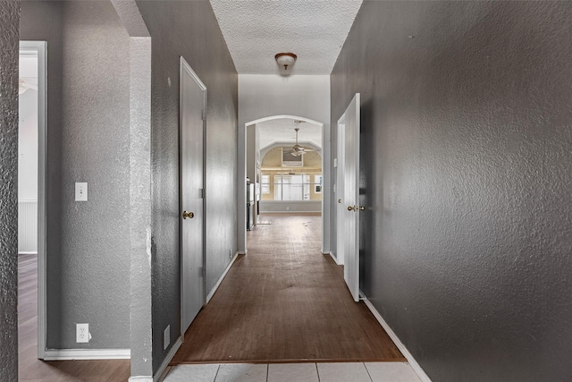 hallway with a textured ceiling, lofted ceiling, and light tile patterned flooring