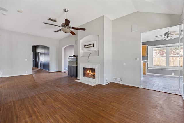 unfurnished living room featuring dark wood-type flooring, lofted ceiling, a tiled fireplace, and ceiling fan