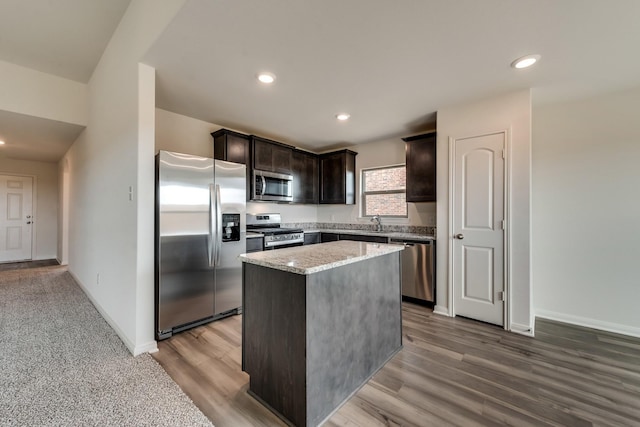 kitchen featuring a center island, sink, dark brown cabinetry, stainless steel appliances, and light stone counters