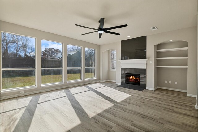 unfurnished living room with hardwood / wood-style flooring, plenty of natural light, built in features, and a tiled fireplace