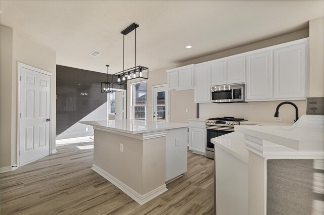 kitchen featuring a kitchen island, light hardwood / wood-style flooring, hanging light fixtures, appliances with stainless steel finishes, and white cabinets