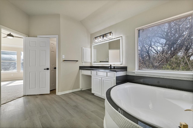 bathroom featuring a washtub, wood-type flooring, vanity, and vaulted ceiling