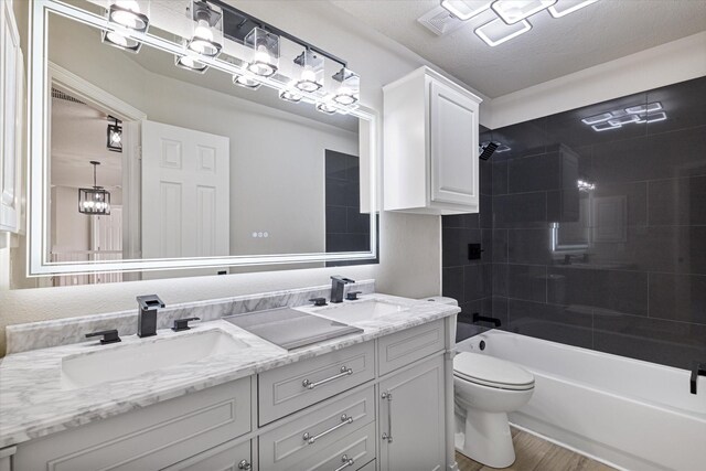 full bathroom featuring hardwood / wood-style floors, tiled shower / bath combo, a textured ceiling, vanity, and toilet