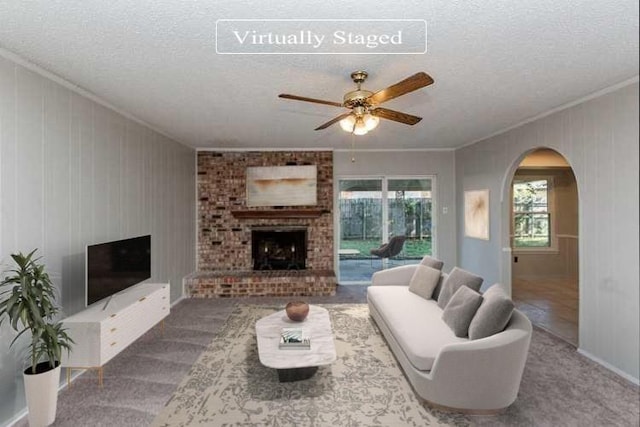 carpeted living room with a textured ceiling, a brick fireplace, ornamental molding, and ceiling fan