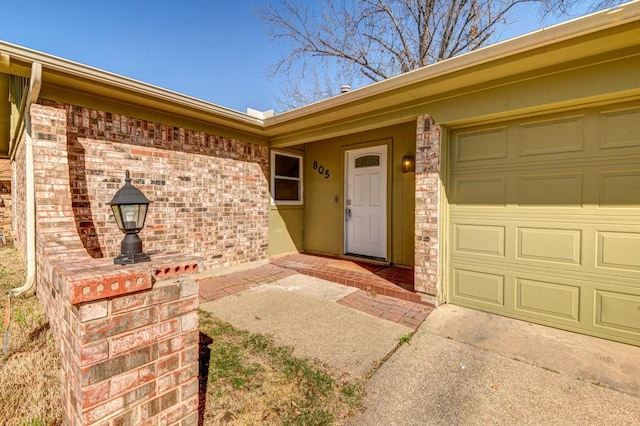 view of exterior entry with a garage and brick siding