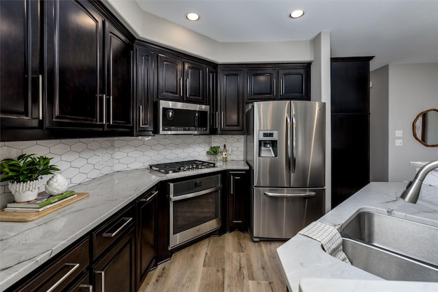 kitchen with stainless steel appliances, backsplash, light wood-type flooring, light stone counters, and sink