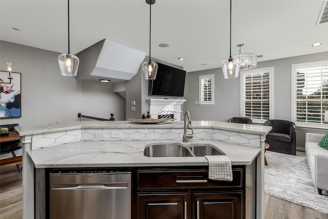 kitchen with light stone countertops, pendant lighting, an island with sink, and sink