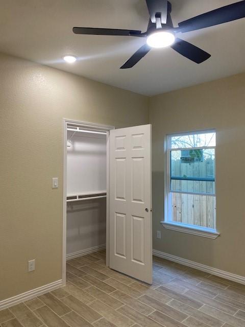 unfurnished bedroom with wood tiled floor, baseboards, ceiling fan, and a closet