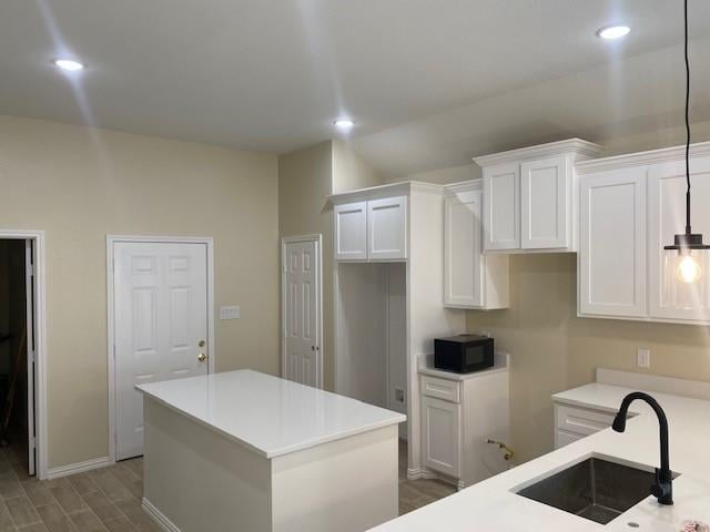 kitchen with white cabinetry, a kitchen island, black microwave, and a sink