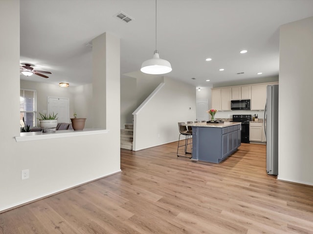 kitchen with a kitchen breakfast bar, hanging light fixtures, a kitchen island, white cabinets, and black appliances