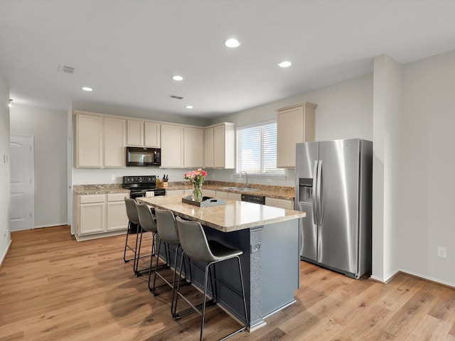 kitchen with a center island, black appliances, light wood-type flooring, light stone countertops, and a breakfast bar area