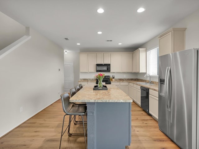 kitchen with black appliances, a kitchen island, a kitchen breakfast bar, sink, and light hardwood / wood-style flooring