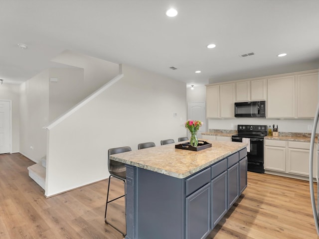 kitchen with white cabinets, black appliances, a center island, a kitchen breakfast bar, and light hardwood / wood-style flooring