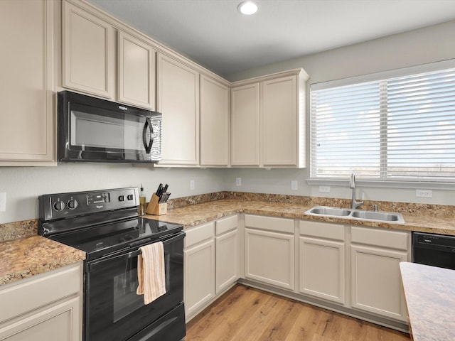 kitchen with sink, light hardwood / wood-style floors, cream cabinets, and black appliances