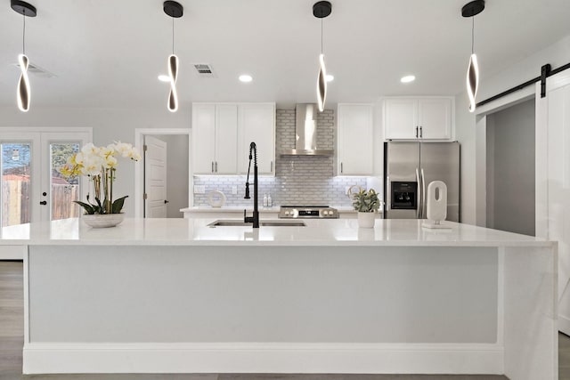 kitchen with a barn door, a large island, appliances with stainless steel finishes, wall chimney range hood, and sink