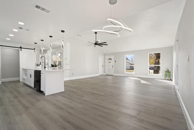 interior space with ceiling fan with notable chandelier, hardwood / wood-style floors, a barn door, and vaulted ceiling