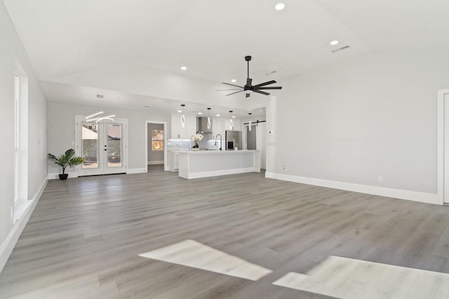 unfurnished living room featuring ceiling fan, a barn door, vaulted ceiling, light hardwood / wood-style flooring, and french doors