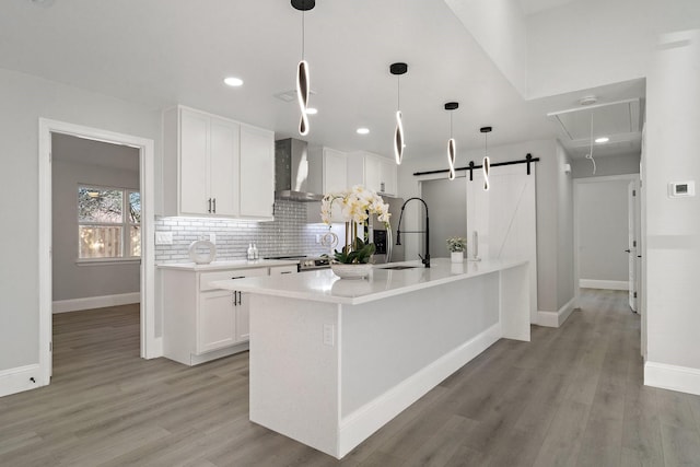 kitchen with decorative light fixtures, a barn door, stainless steel stove, white cabinetry, and wall chimney exhaust hood