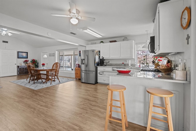 kitchen with white cabinets, lofted ceiling, stainless steel refrigerator with ice dispenser, a kitchen breakfast bar, and light hardwood / wood-style flooring