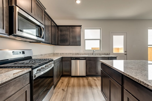 kitchen featuring light wood-type flooring, dark brown cabinets, light stone counters, and stainless steel appliances