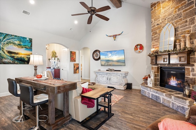 living room featuring ceiling fan, dark hardwood / wood-style floors, beam ceiling, and a stone fireplace