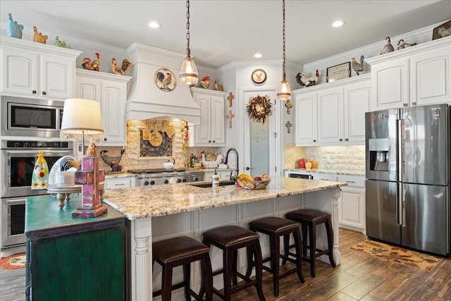 kitchen with white cabinets, stainless steel appliances, an island with sink, decorative backsplash, and sink