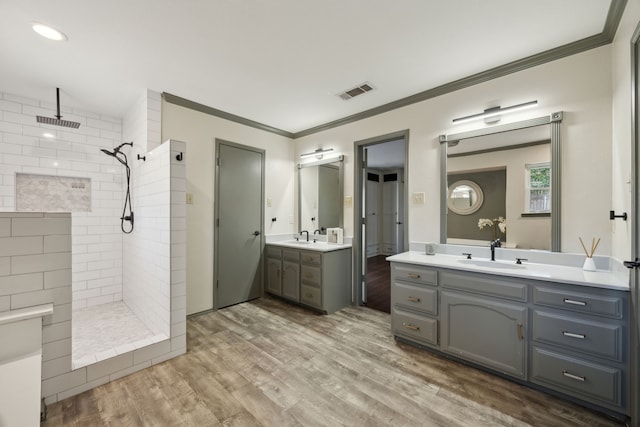 bathroom with vanity, wood-type flooring, crown molding, and a tile shower