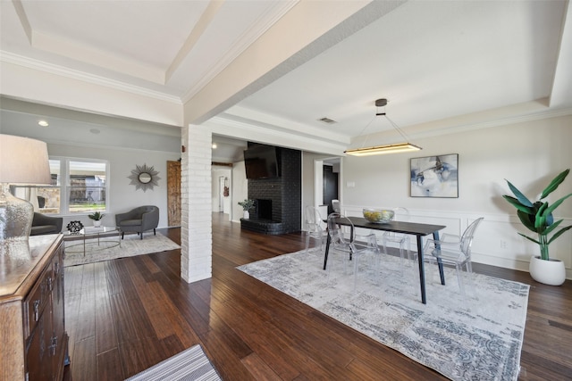 dining area with a brick fireplace, a tray ceiling, dark hardwood / wood-style floors, and ornate columns