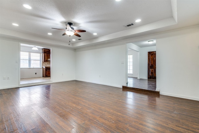 unfurnished living room featuring a tray ceiling, dark wood-type flooring, a textured ceiling, and ceiling fan