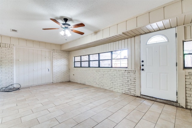 foyer entrance with ceiling fan, brick wall, and a textured ceiling