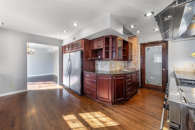 kitchen featuring dark wood-type flooring, dark stone countertops, sink, backsplash, and stainless steel refrigerator