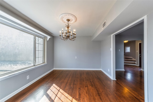 spare room with dark hardwood / wood-style flooring and an inviting chandelier