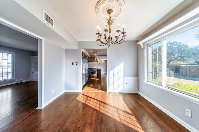 unfurnished dining area featuring a chandelier, a healthy amount of sunlight, and dark hardwood / wood-style flooring