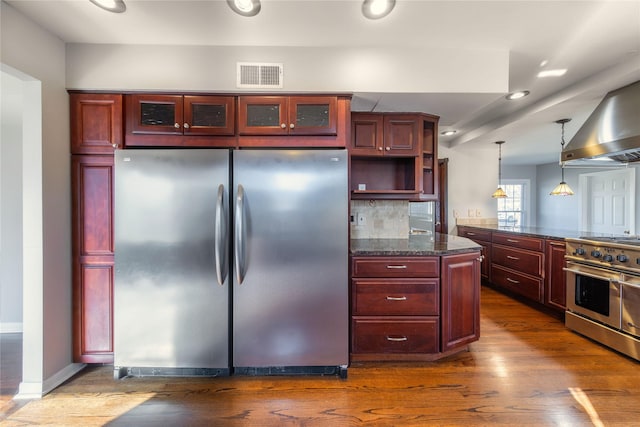 kitchen with appliances with stainless steel finishes, decorative light fixtures, dark hardwood / wood-style flooring, dark stone countertops, and backsplash